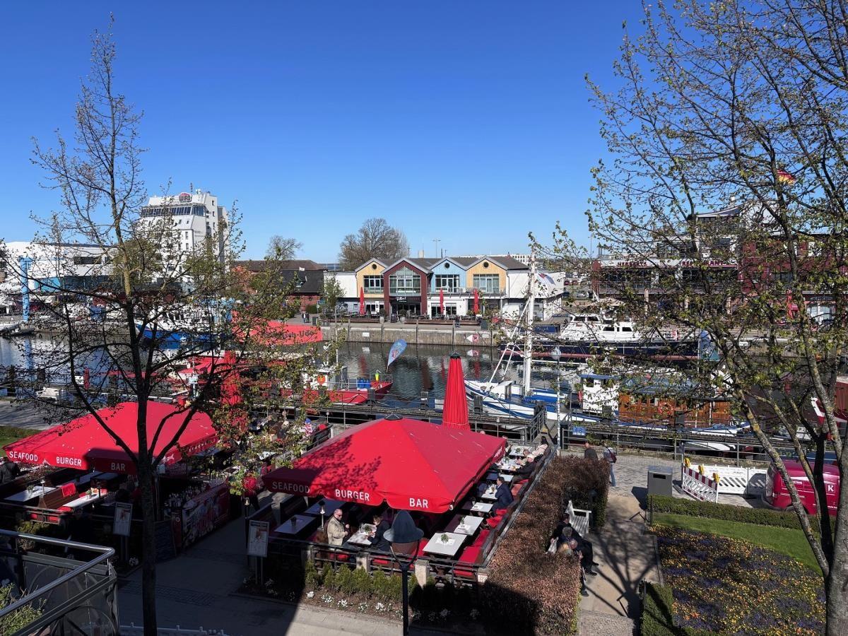 Roter Sonnenschirm über Terrasse mit Blick auf Hafen und Boote.