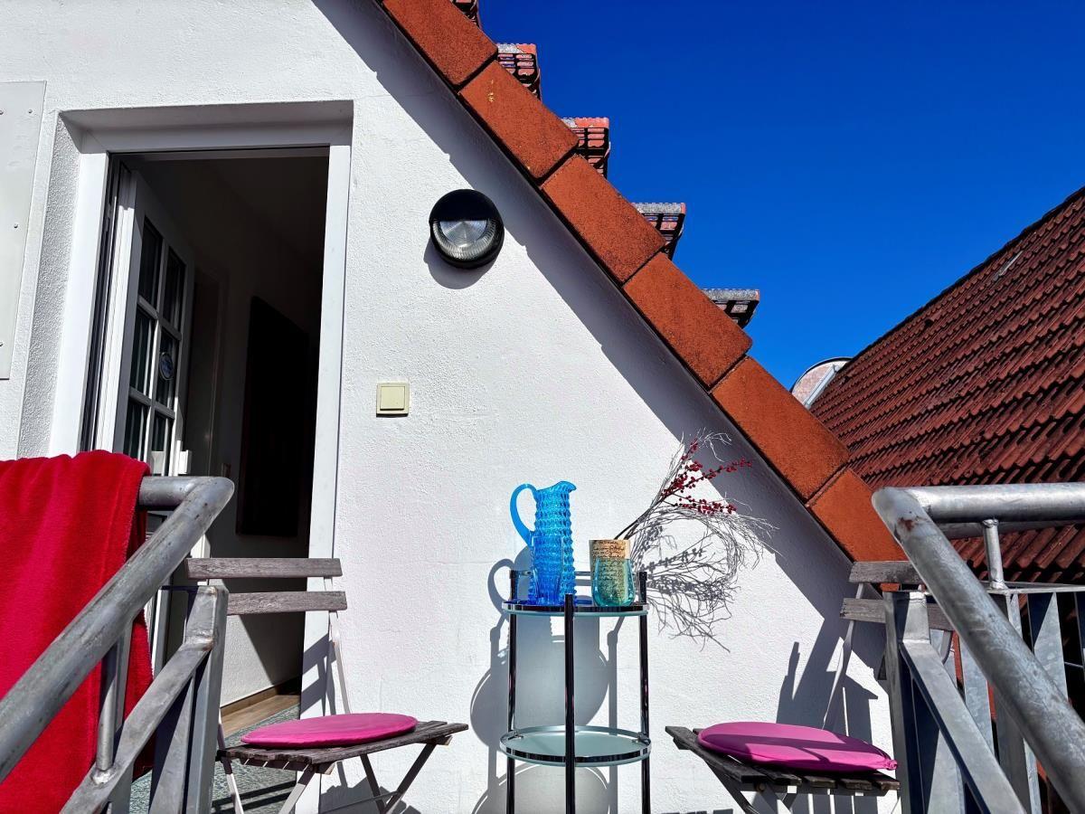 Terrasse mit Tisch, zwei Stühlen und rotem Handtuch. Hintergrund: weißer Hauswandschatten und rote Dachziegel.