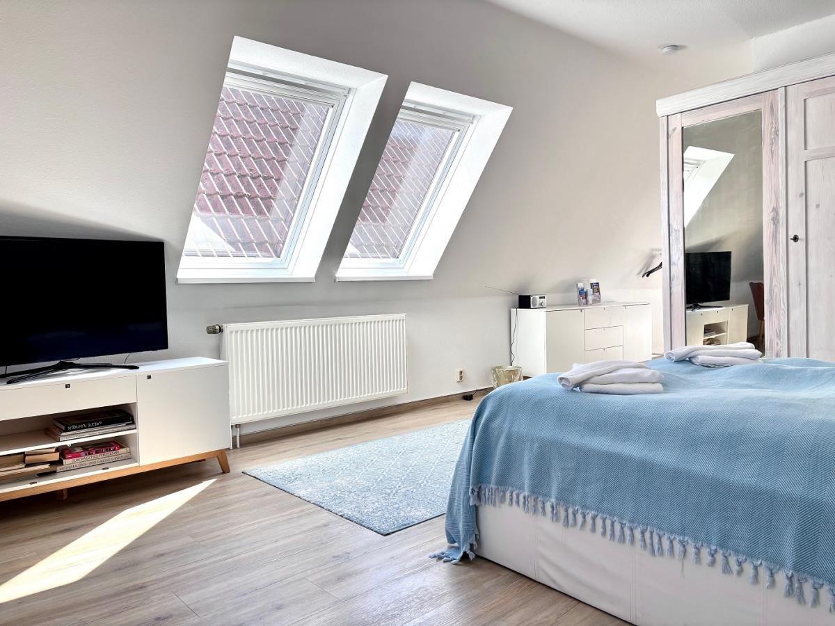 Schlafzimmer mit Dachfenstern, Bett mit blauer Tagesdecke und Fernseher auf weißen Schränken.