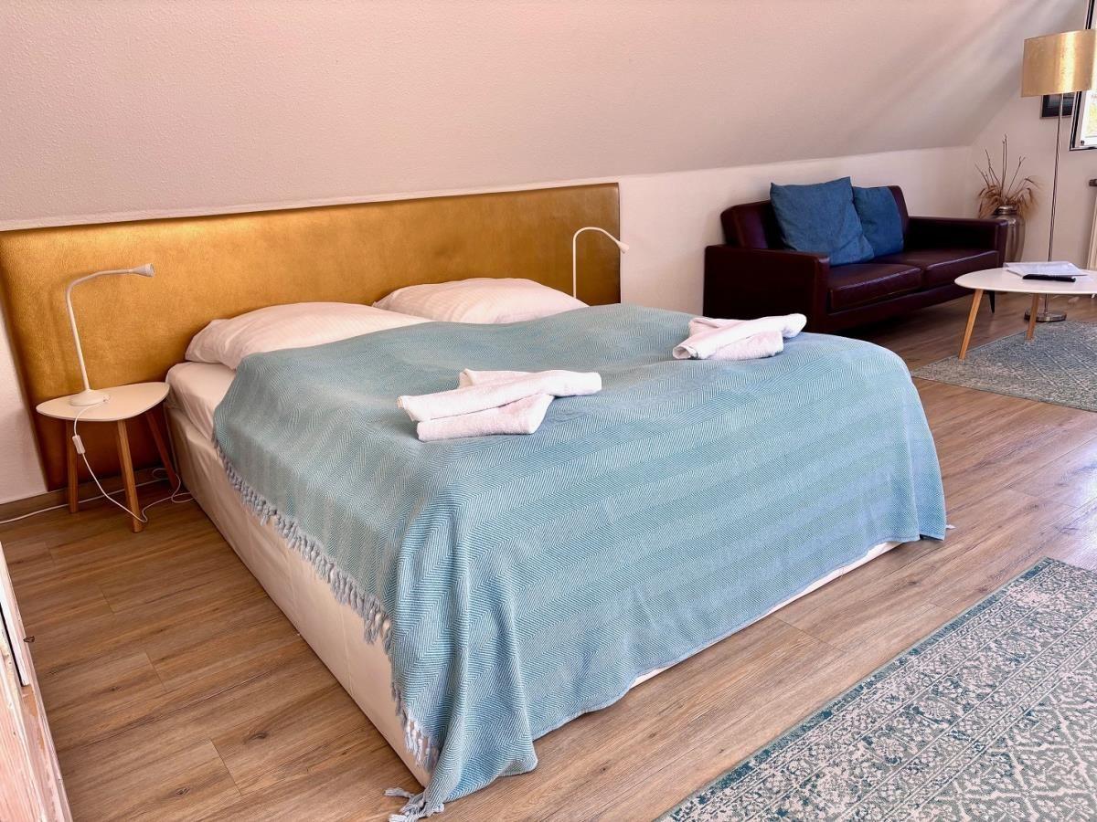 Schlafzimmer mit Doppelbett, goldfarbener Kopfseite und braunem Sofa.