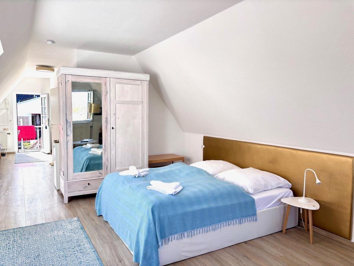 Schlafzimmer mit Dachschrägen, Bett mit blauer Tagesdecke, Spiegelschrank und Nachttisch.