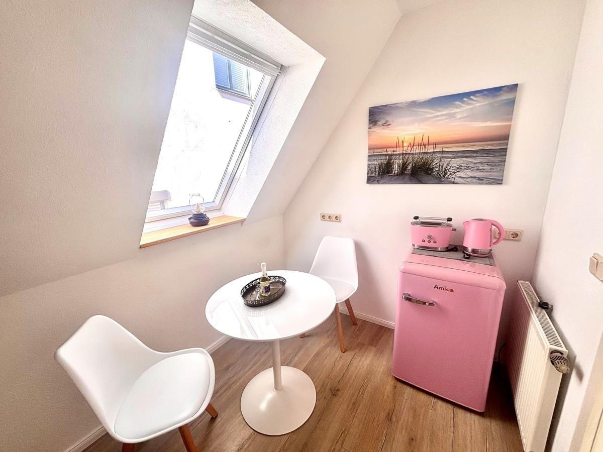 Kleiner Raum mit rosa Kühlschrank, Tisch, zwei Stühlen und Dachfenster.
