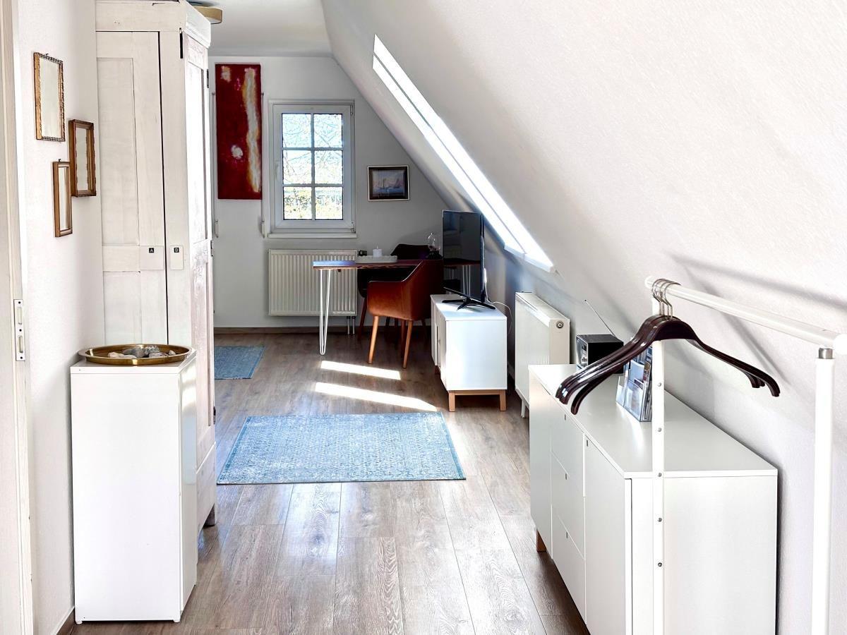 Schlafzimmer mit Dachschräge, Schreibtisch, TV und Kleiderschrank.