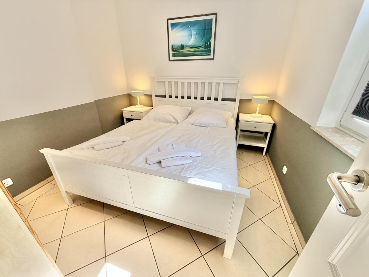Schlafzimmer mit weißem Bett, zwei Nachttischen und Wandbild.
