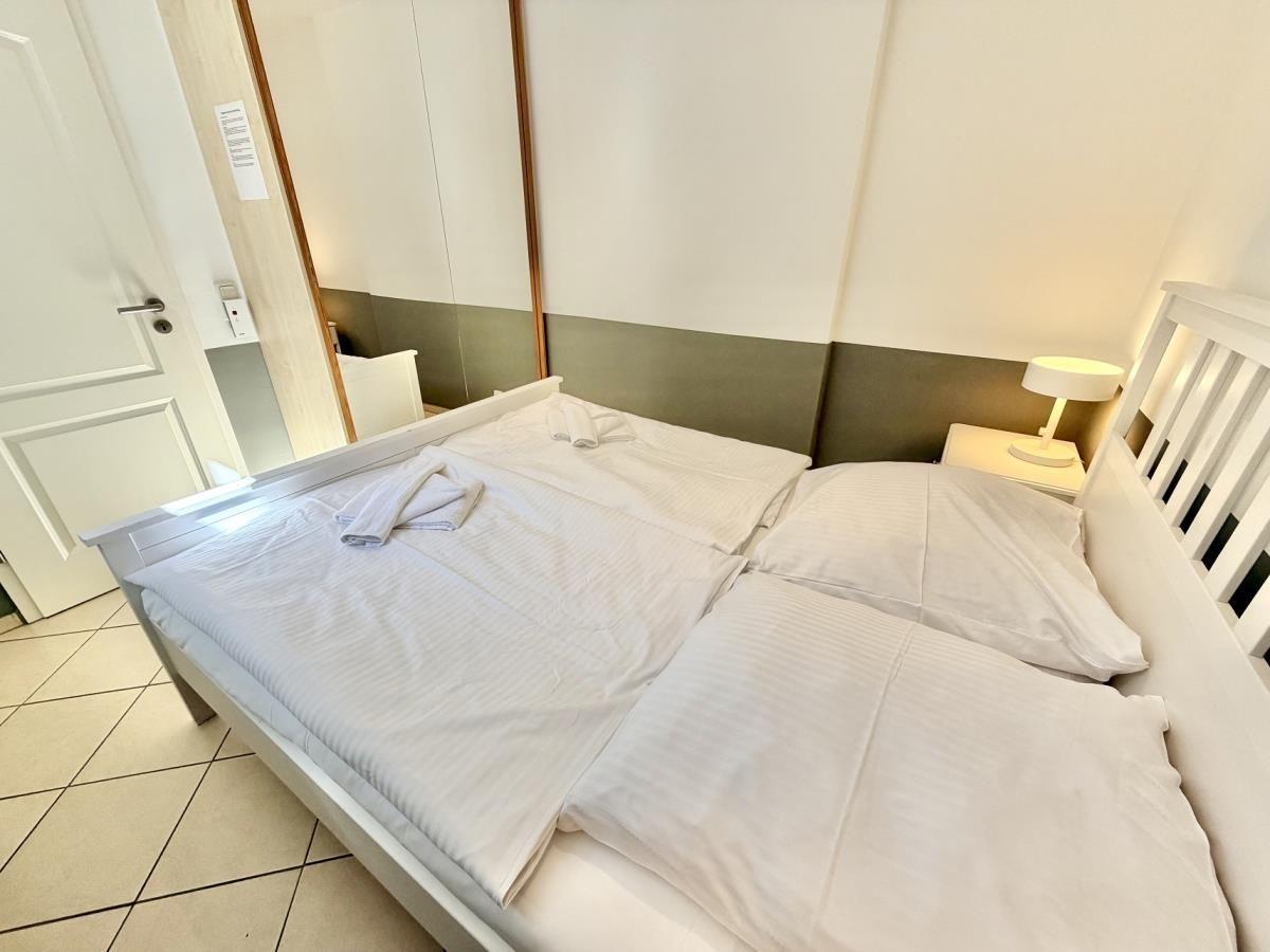 Schlafzimmer mit Doppelbett, Nachttisch und Lampe. Fliesenboden und Spiegelschrank.