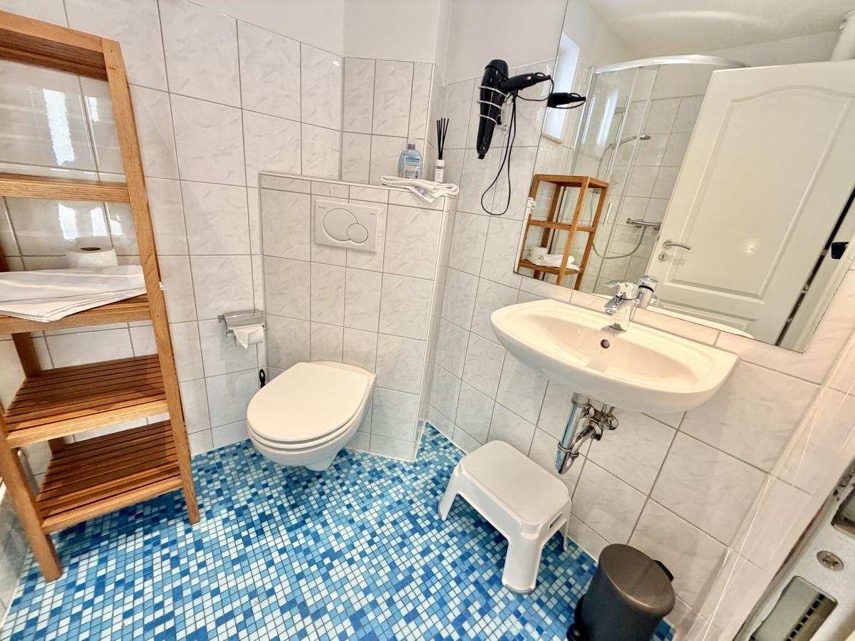 Badezimmer mit blauem Mosaikboden, Toilette, Waschbecken und Dusche.