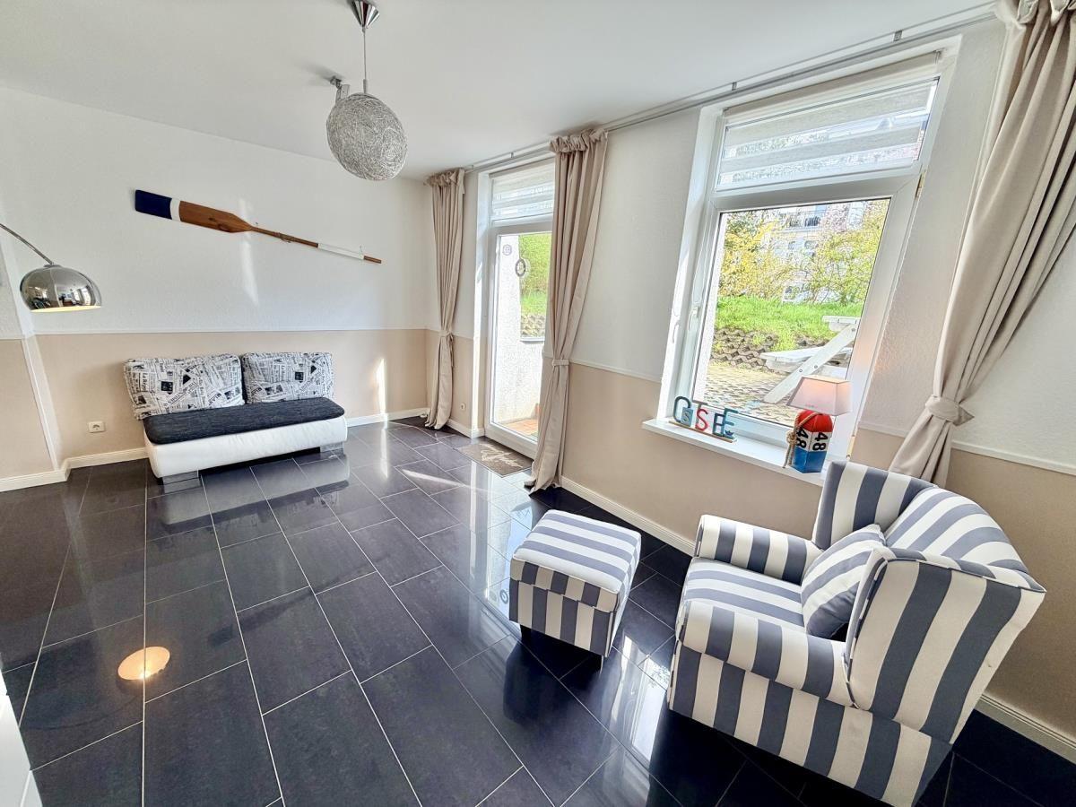 Wohnraum mit Sofa, Sessel und Fenster mit Blick nach draußen.