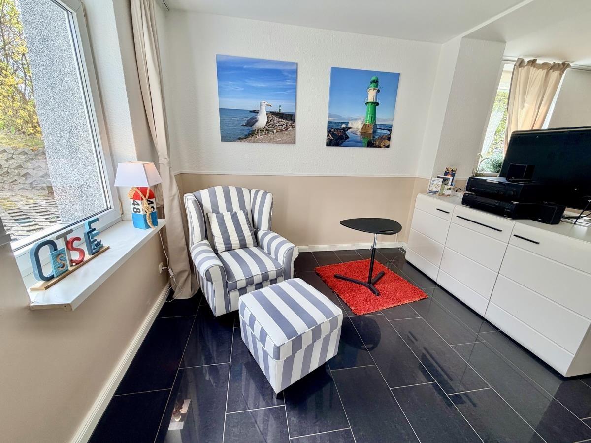 Wohnzimmer mit Sessel, Fußhocker und Fernseher. Wandbilder zeigen Leuchtturm und Seemöwen.