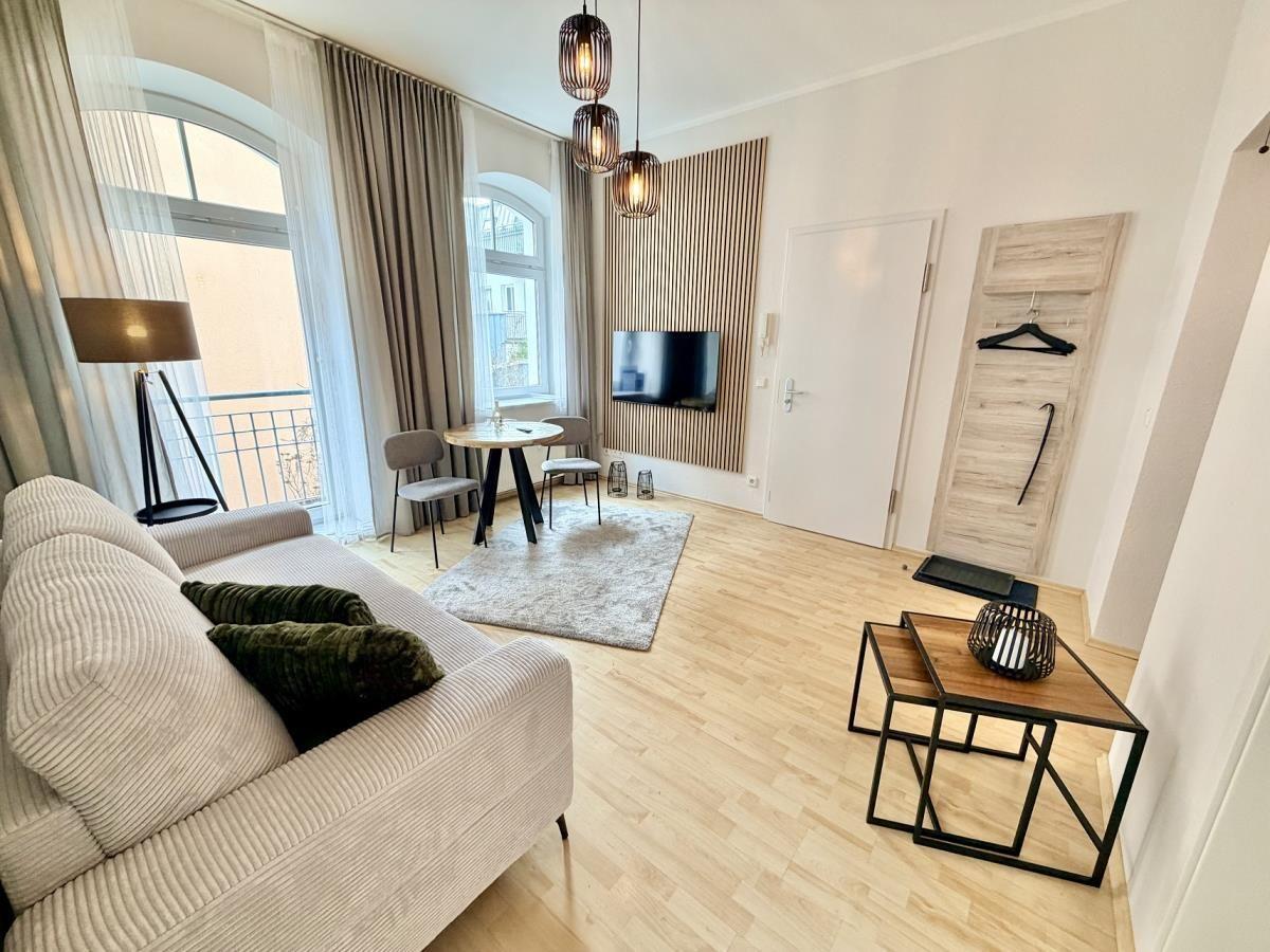 Wohnzimmer mit Sofa, Esstisch, TV und Balkonzugang.