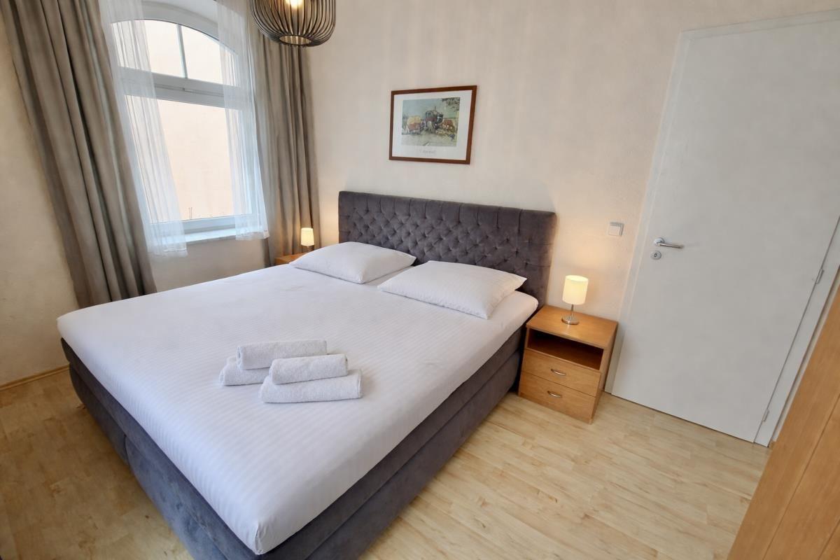 Schlafzimmer mit Doppelbett, Nachttisch und Fenster mit Vorhängen.