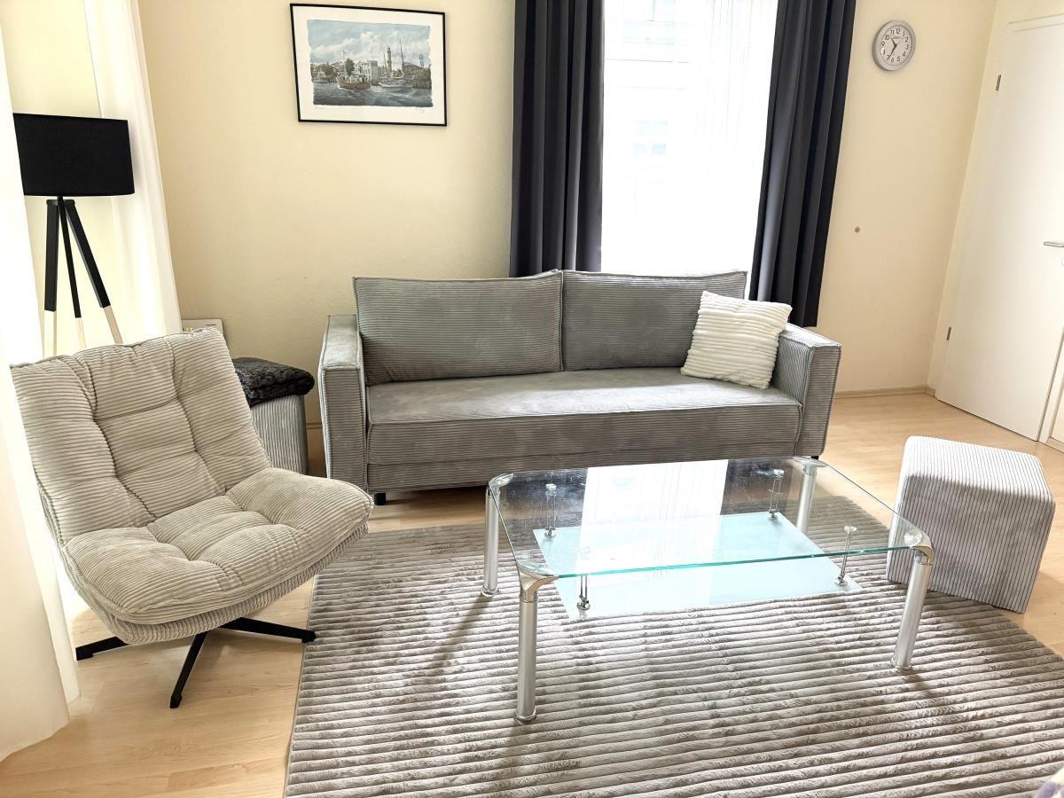 Wohnzimmer mit Sofa, Sessel, Glas-Tisch und Teppich