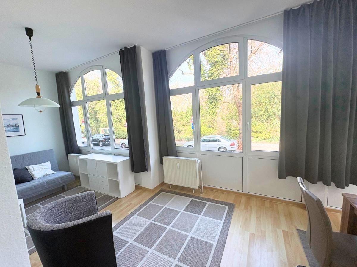 Wohnzimmer mit großem Fenster, Sofa, Stuhl und Teppich auf Holzboden.