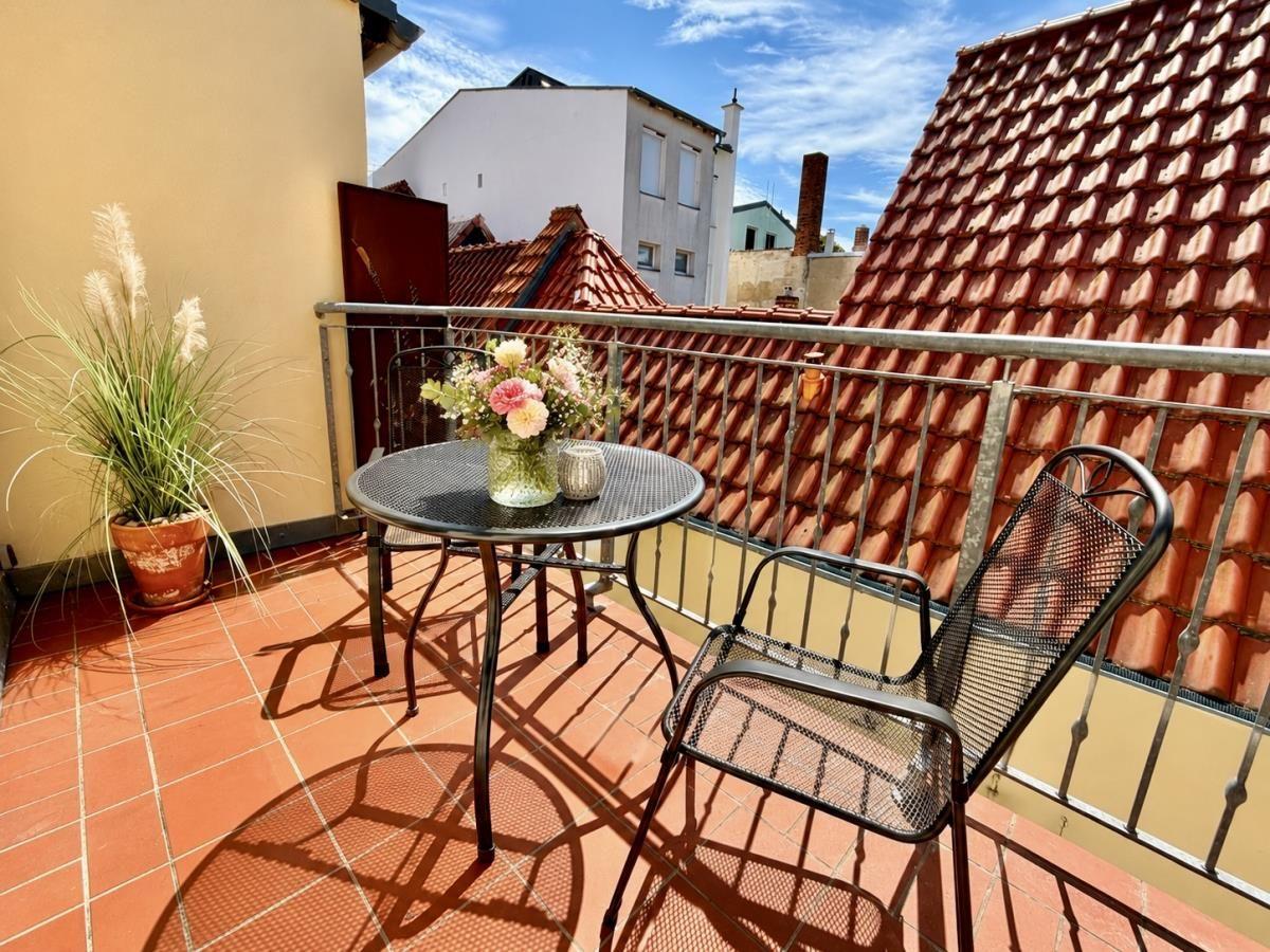 Terrasse mit Tisch, zwei Stühlen und Pflanze. Blick auf rote Dächer und Himmel.