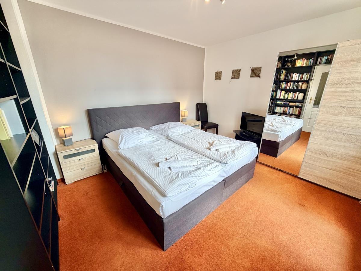 Schlafzimmer mit Doppelbett, Nachttisch, Spiegel und Bücherregal.