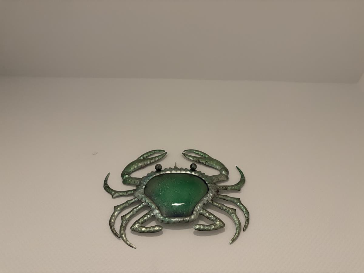 Metallkunstwerk in Form eines Krabbenmotivs mit grünem Stein in der Mitte an der Wand