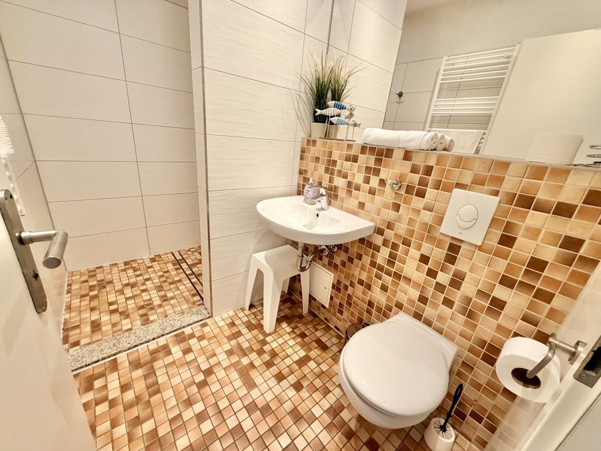 Badezimmer mit Toilette, Waschbecken und Dusche. Fliesenwand und Boden mit Mosaikfliesen.