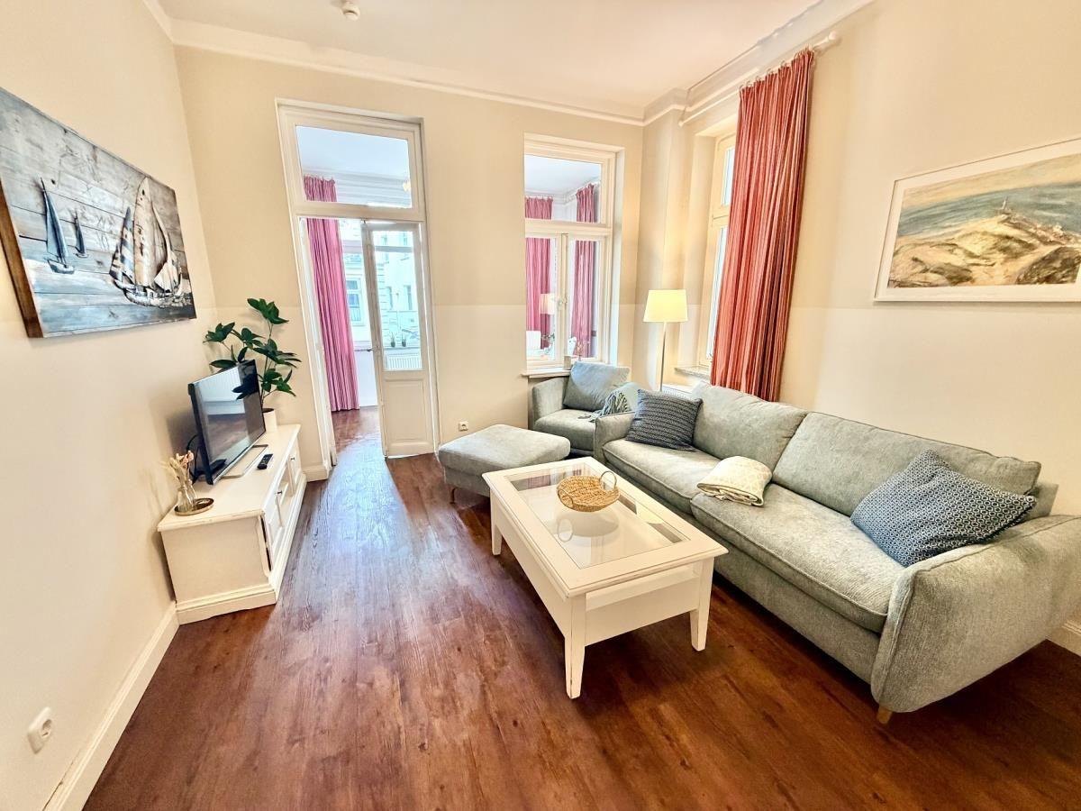 Wohnzimmer mit Sofa, Couchtisch und Holzboden. Fenster mit roten Vorhängen.
