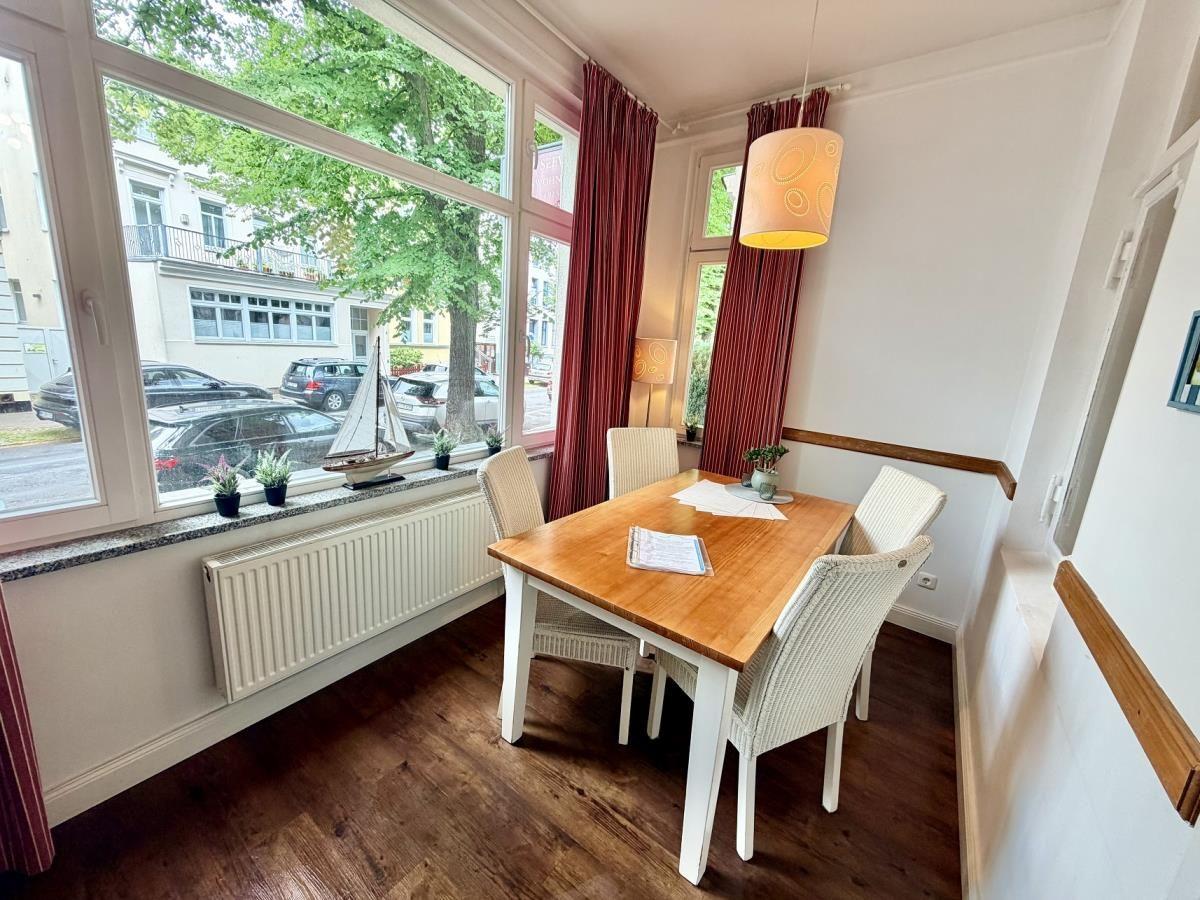 Esszimmer mit Holztisch, Stühlen und großem Fenster. Rote Vorhänge und Lampe.