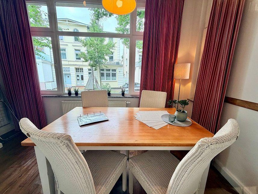 Esszimmer mit Holztisch, vier Stühlen und großem Fenster mit Blick auf Straße.