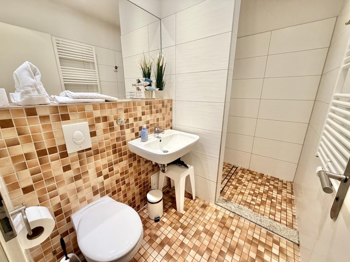 Badezimmer mit Toilette, Waschbecken und Dusche. Wand- und Bodenfliesen in warmen Tönen.