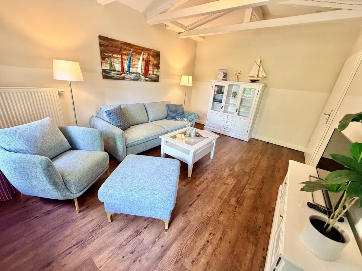 Wohnzimmer mit Sofa, Sessel und Holzboden. Wandbild und Schrank sind sichtbar.