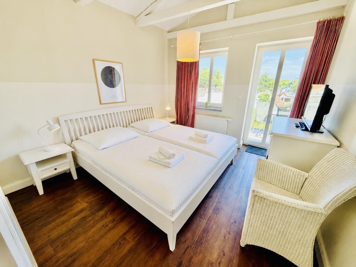 Schlafzimmer mit Doppelbett, Schreibtisch und Balkontür.
