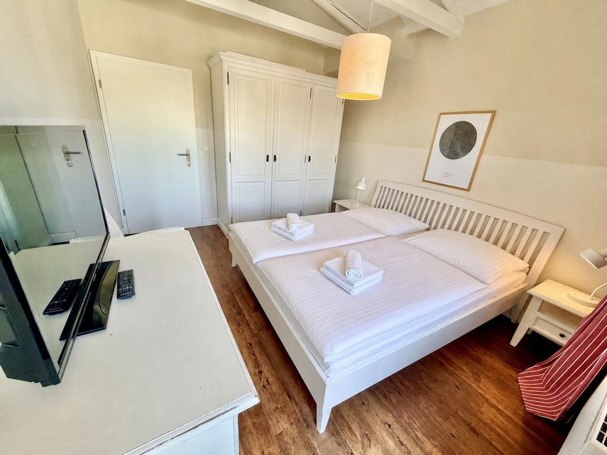 Schlafzimmer mit weißem Bett, Schrank und Holzboden. Fernseher auf Tisch.