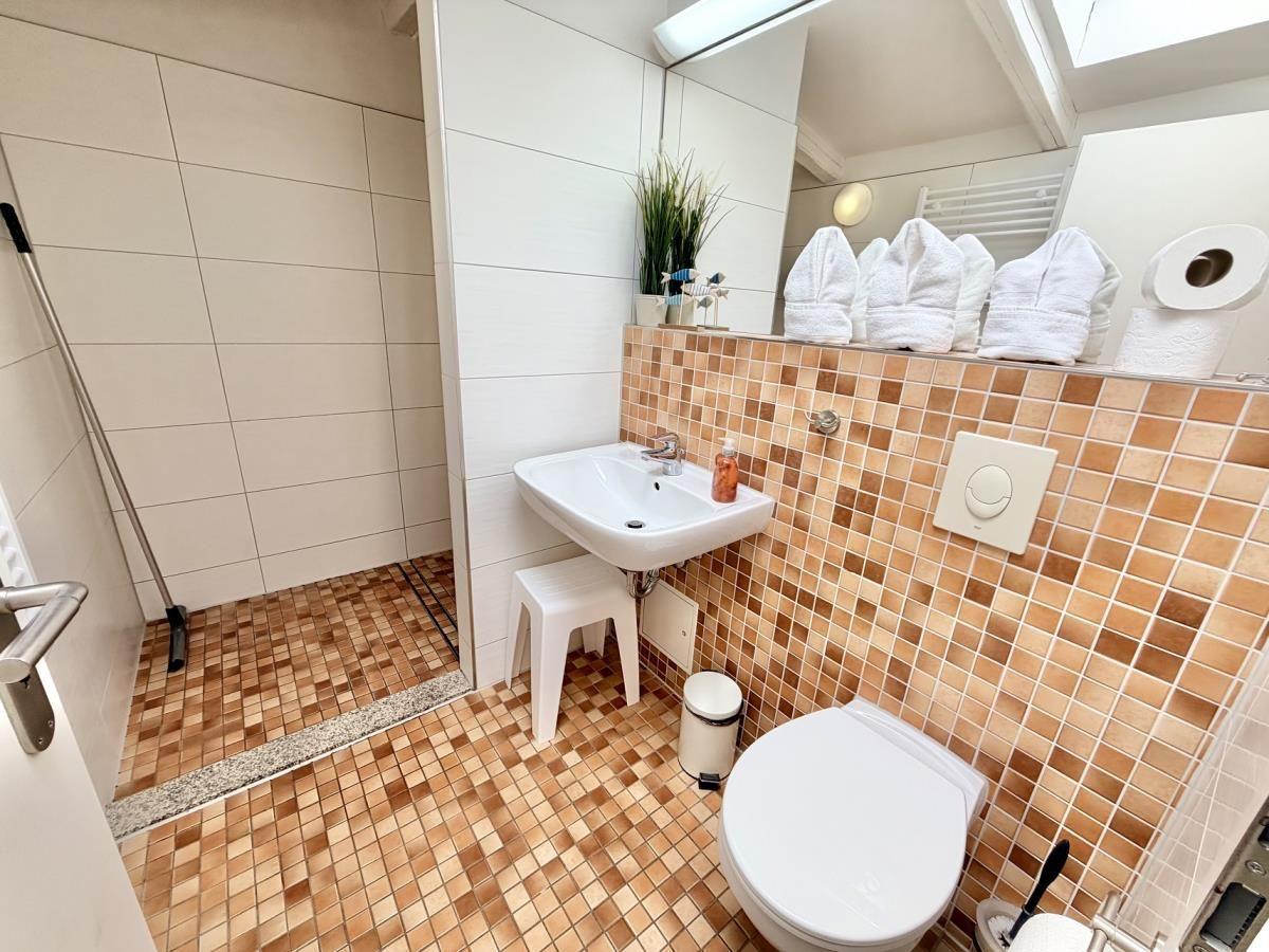 Badezimmer mit Dusche, Waschbecken und Toilette. Fliesenboden und -wände.