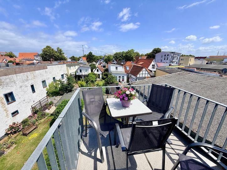 Terrasse mit Tisch, Stühlen und Blumen, Blick auf Dächer und Grünflächen.