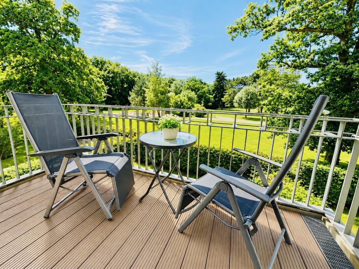 Terrasse mit zwei Liegestühlen und Tisch, Blick auf grünen Park.