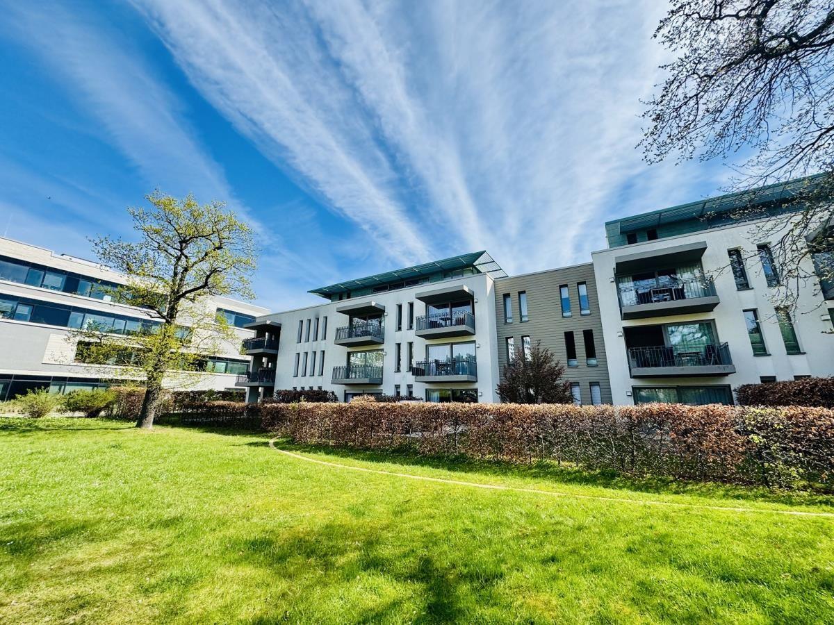 Moderne Wohnanlage mit Balkonen und grünem Rasenbereich unter blauem Himmel.