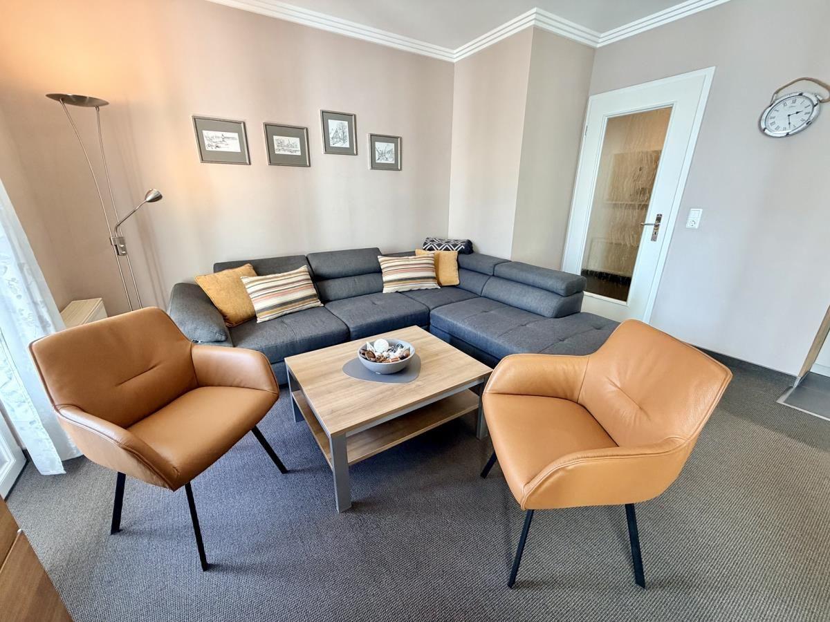 Ein Wohnzimmer mit grauem Sofa, zwei braunen Sesseln und einem Holztisch.