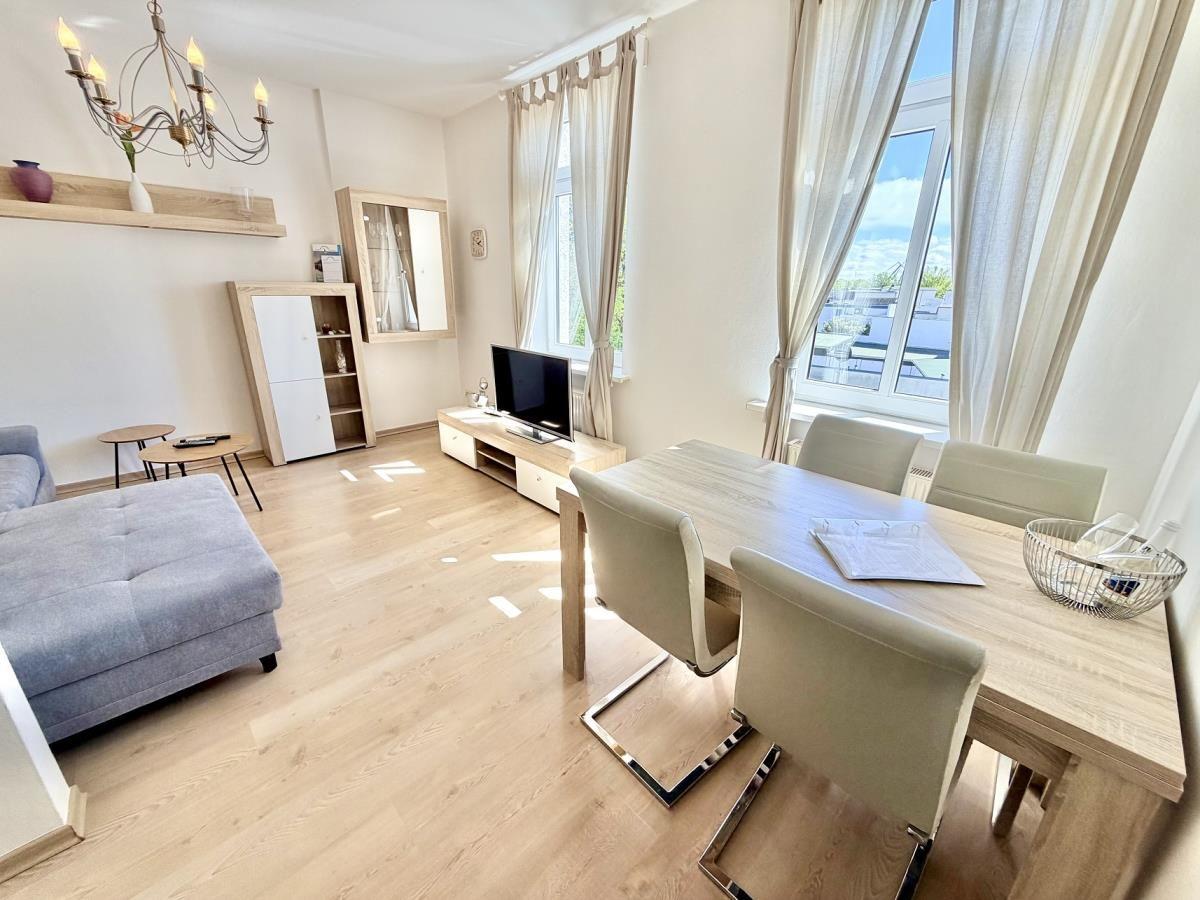Wohn- und Essbereich mit Holzboden, TV, Tisch und Stühlen sowie großen Fenstern.