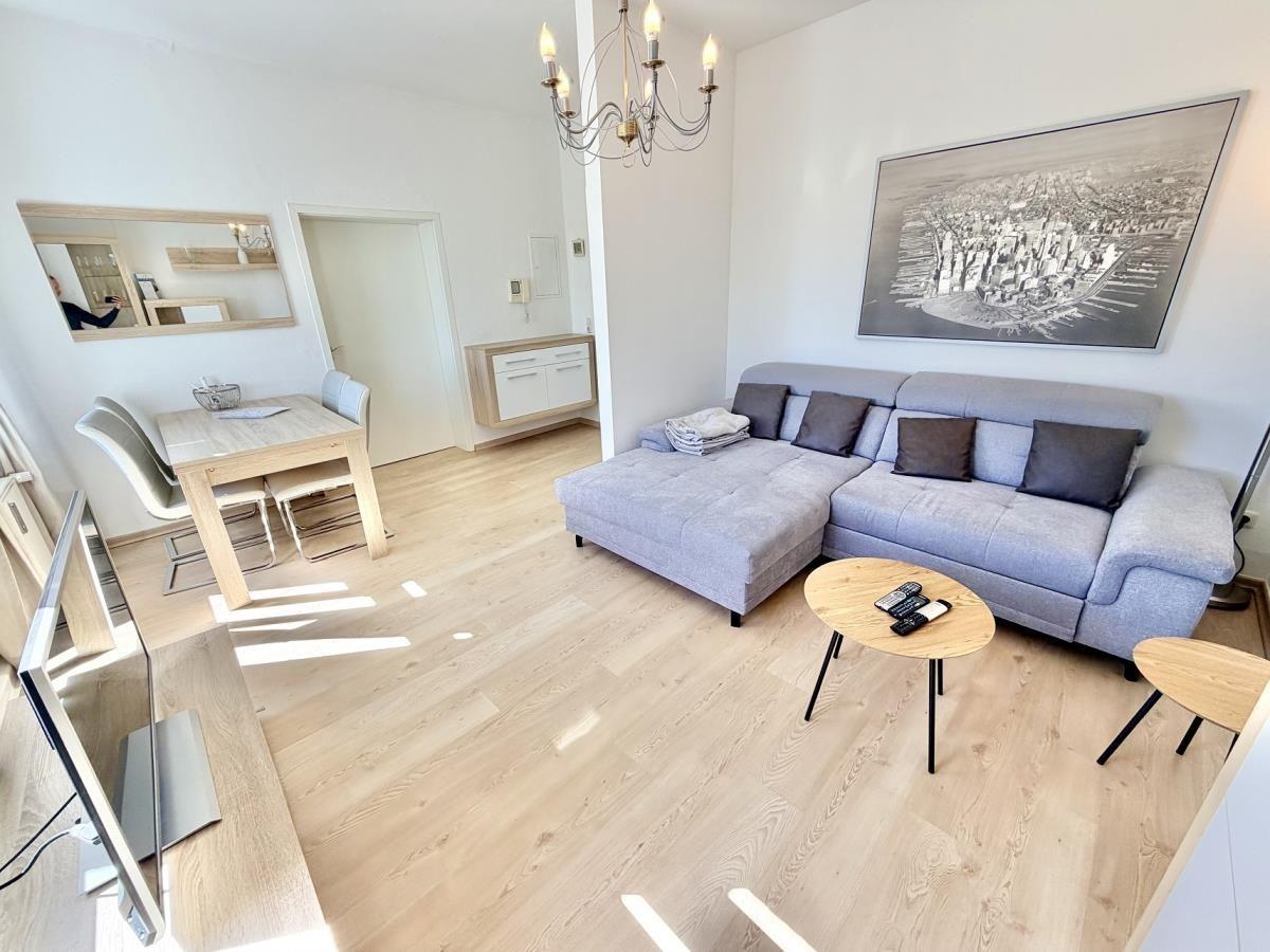 Wohnzimmer mit Sofa, Esstisch und Kronleuchter. Holzfußboden und Wandbild.