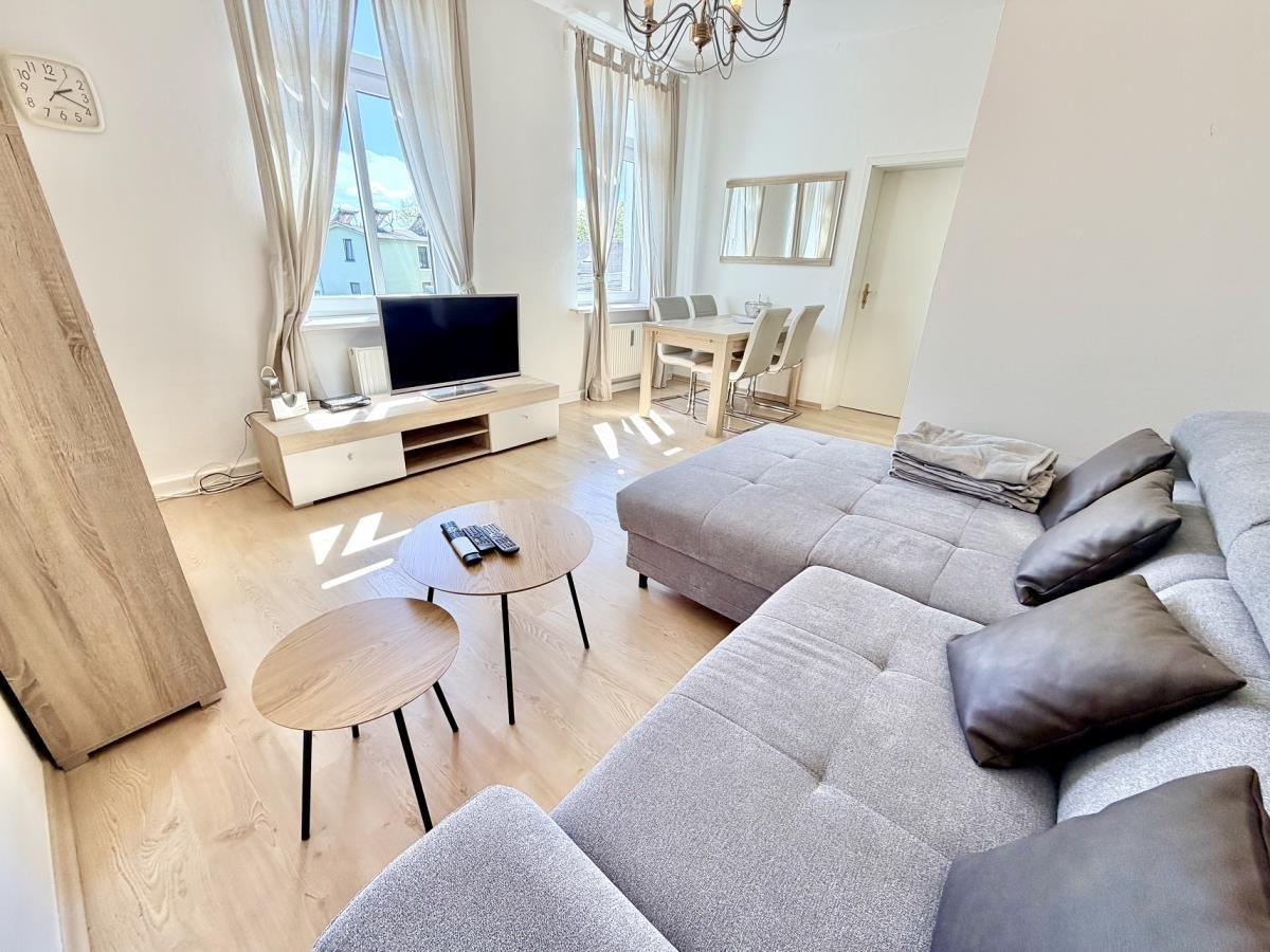 Wohnzimmer mit Sofa, Fernseher und Essbereich mit Tisch und Stühlen.