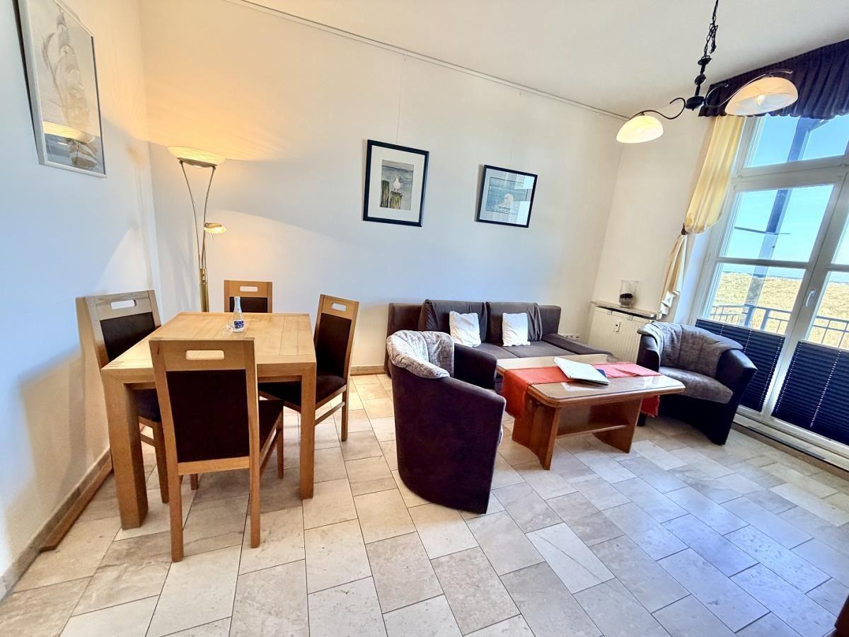 Wohn- und Essbereich mit Sofa, Tisch und Stühlen. Große Fenster mit Blick auf Balkon.