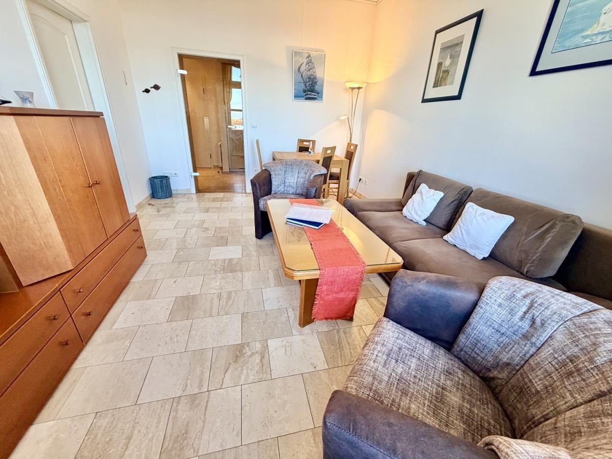 Wohnzimmer mit Sofa, Couchtisch und Holzmöbeln. Fliesenboden und Wandbilder.