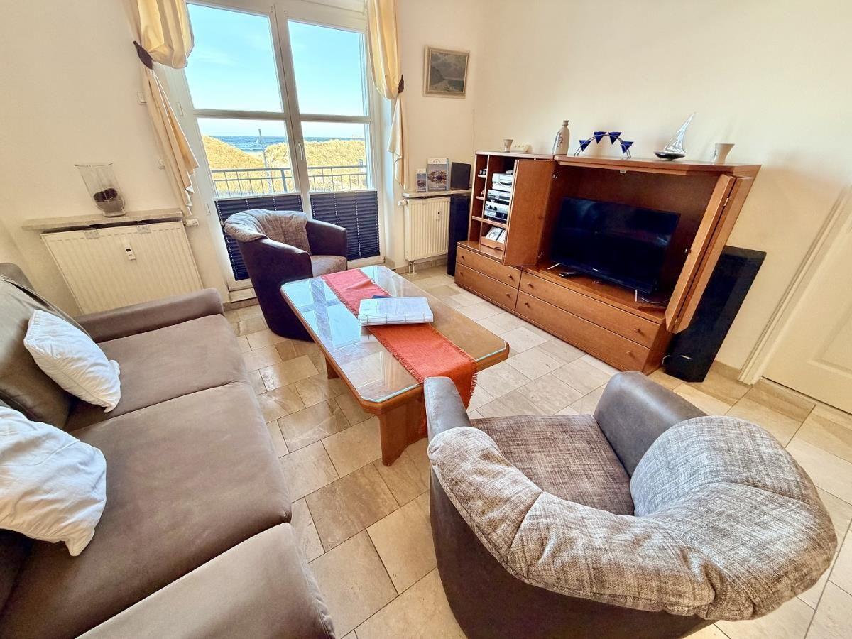 Wohnzimmer mit Sofa, Sessel und TV-Schrank. Blick aufs Meer durch Fenster.