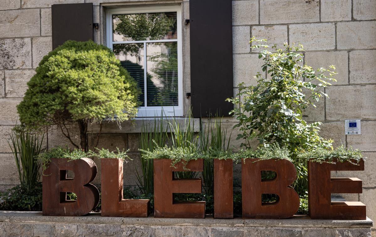 Vorderseite mit Steinmauer, Fenster und großen Buchstaben BLEIBE