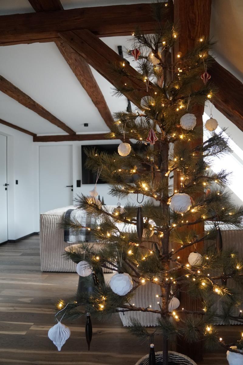 Weihnachtsbaum mit Lichtern und Dekorationen in einem Raum mit Holzbalken und Fernseher.