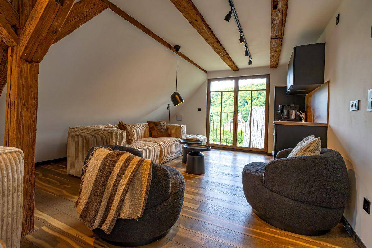 Wohnraum mit Holzbalken, Sofa, zwei Sessel und Blick auf Balkon