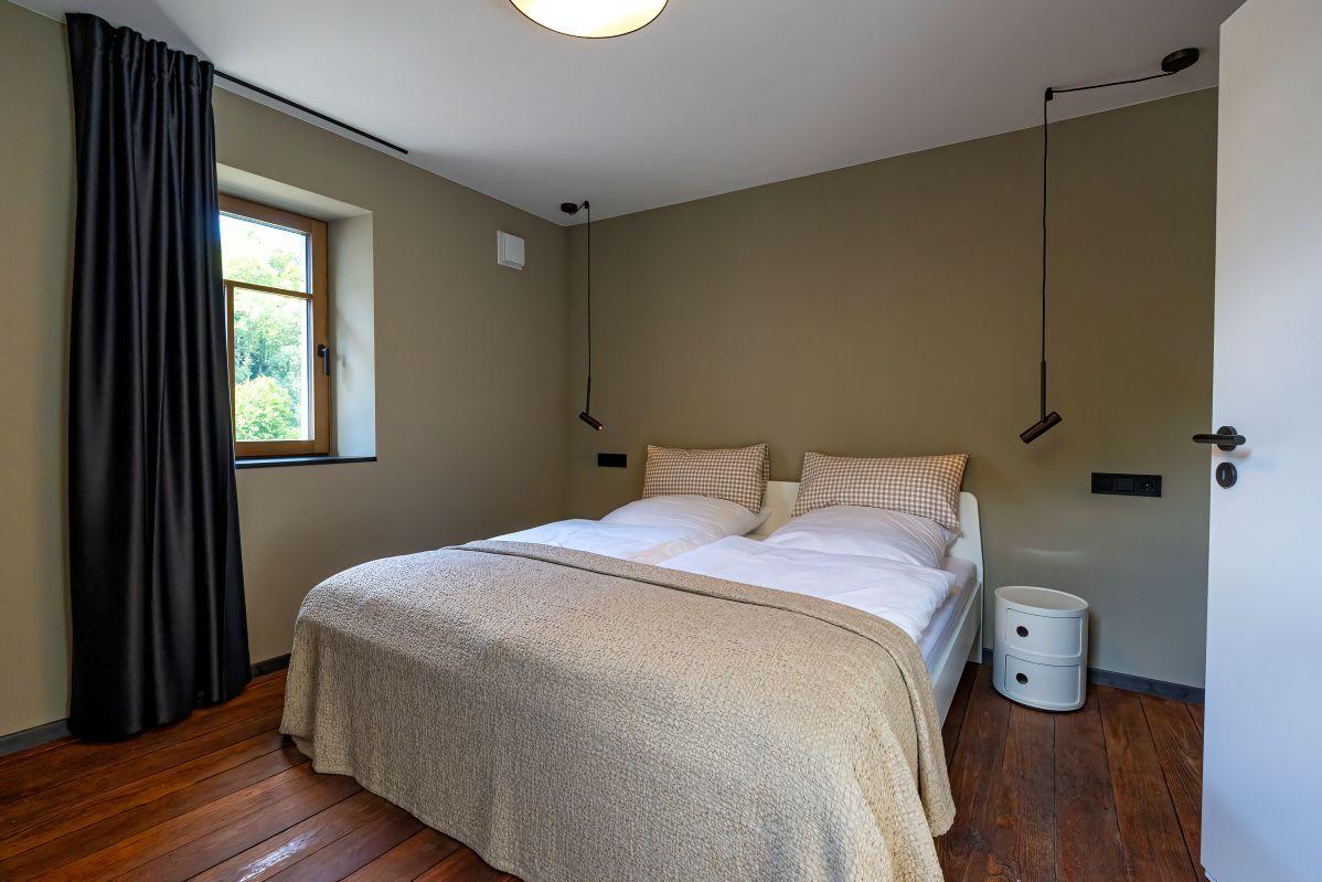 Schlafzimmer mit Doppelbett, Holzboden und Fenster mit Blick auf Grün.