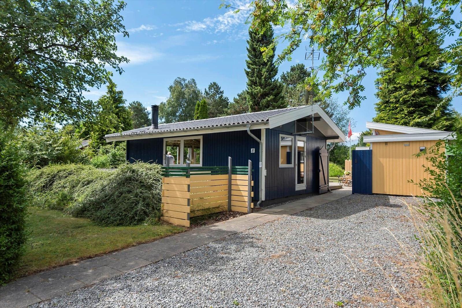 Ein blaues Ferienhaus mit Holzverkleidung und Garten. Ein Tor führt zum Eingang.