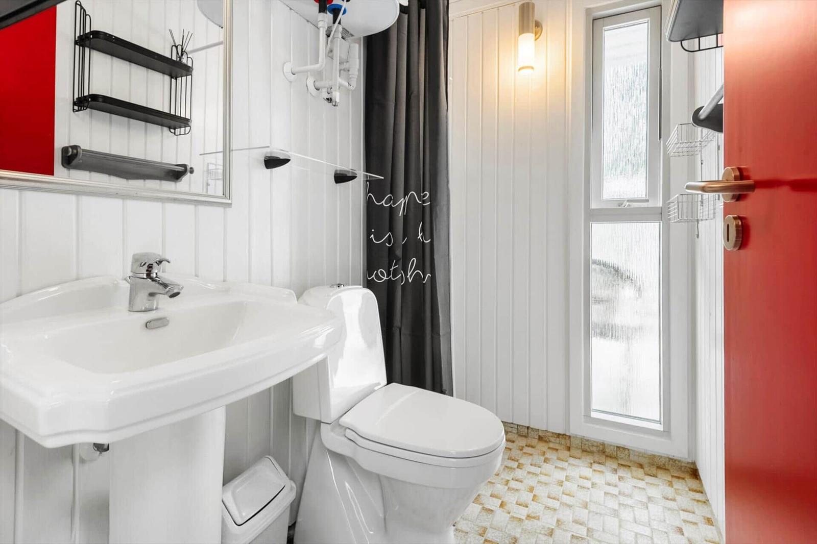Badezimmer mit Toilette, Waschbecken und Duschkabine mit Fenster.