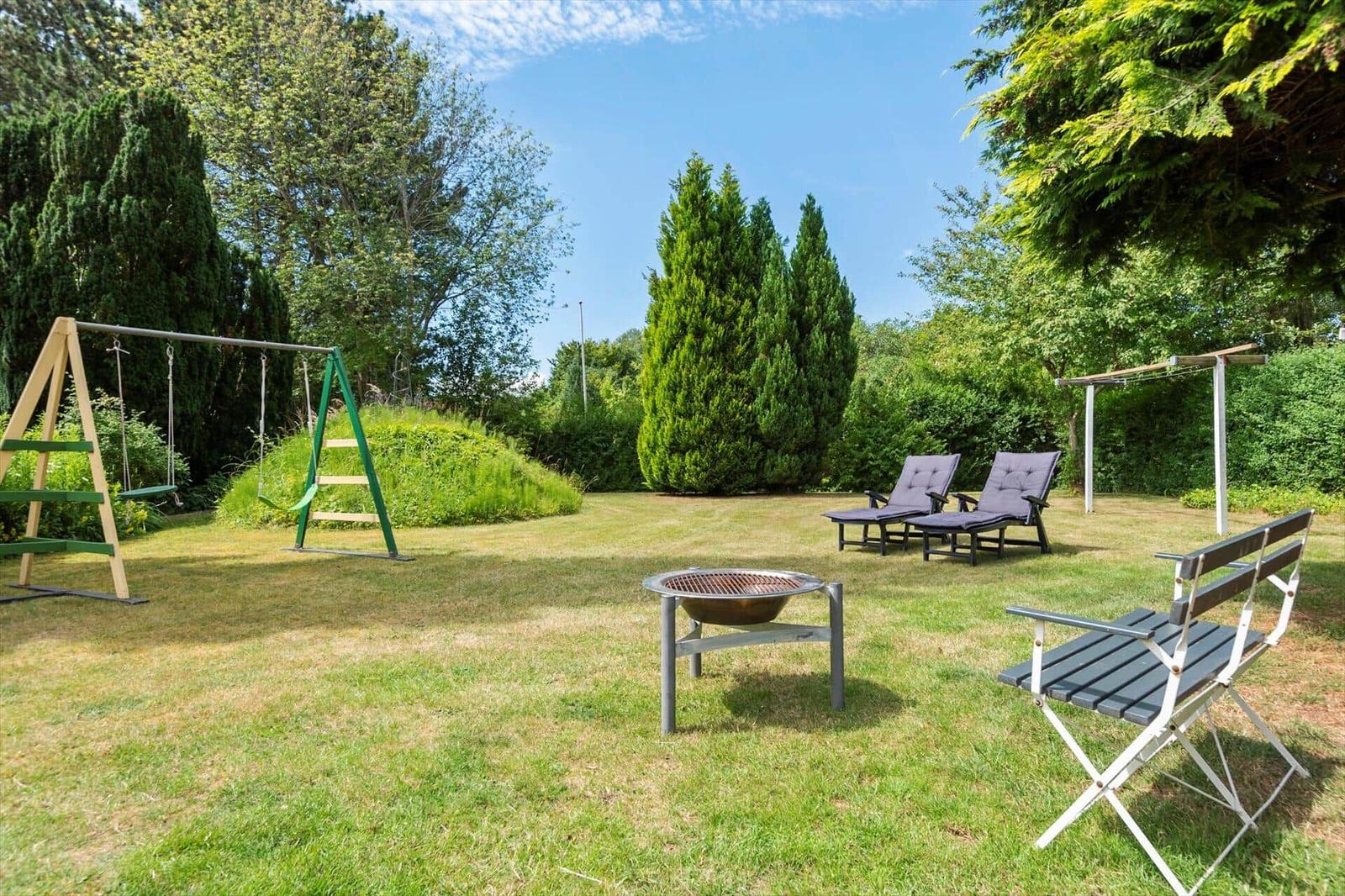Grüner Garten mit Schaukel, Liegestühlen und Grillplatz.