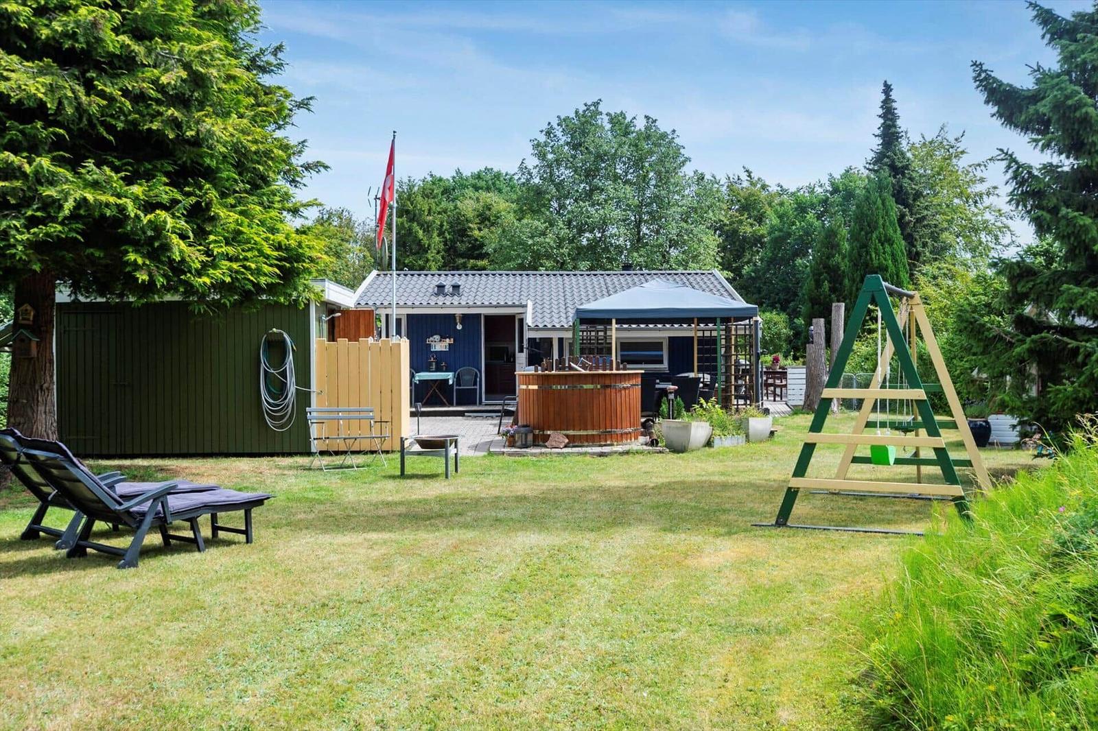 Haus mit Garten, Whirlpool, Liegestühle und Schaukel. Umgeben von Bäumen und Gras.