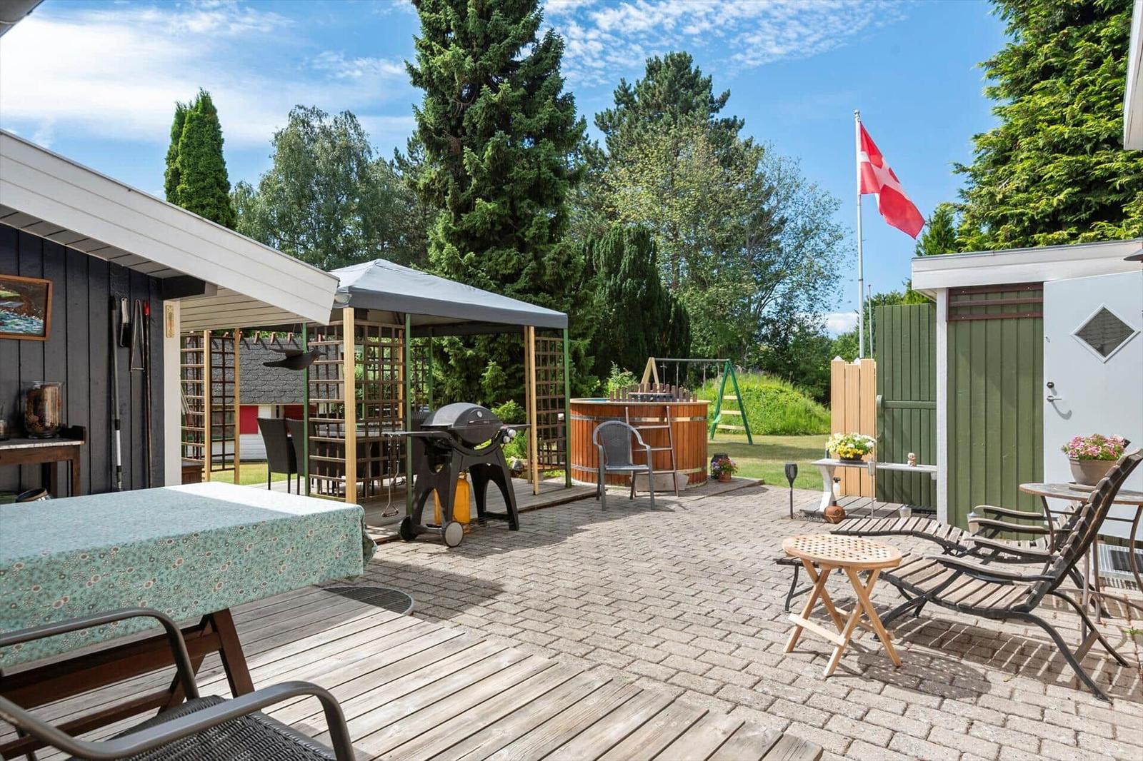 Terrasse mit Grill, Whirlpool und Gartenmöbeln unter blauem Himmel.