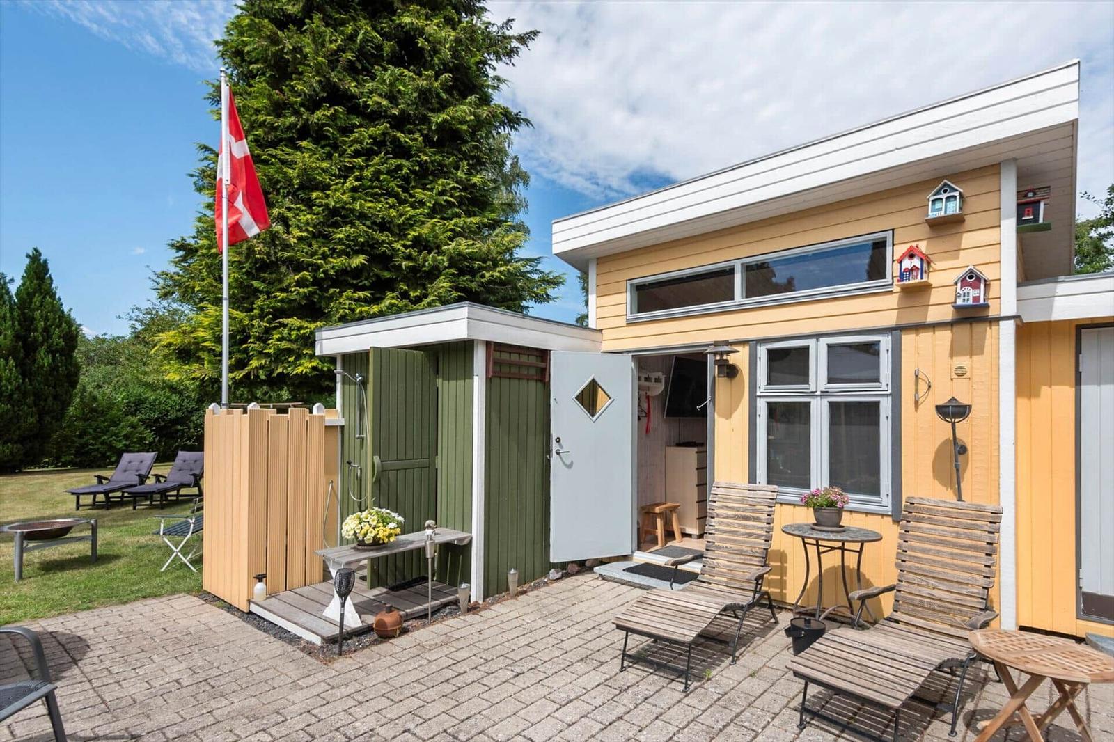 Haus mit Terrasse, Außendusche und Garten. Daneben steht eine Flagge.