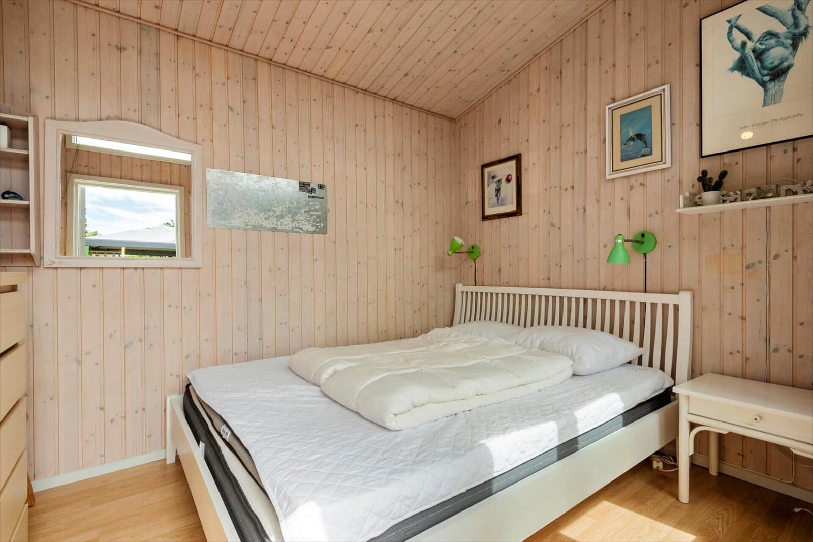 Schlafzimmer mit Holzwand, weißem Bett und grünen Wandlampen.