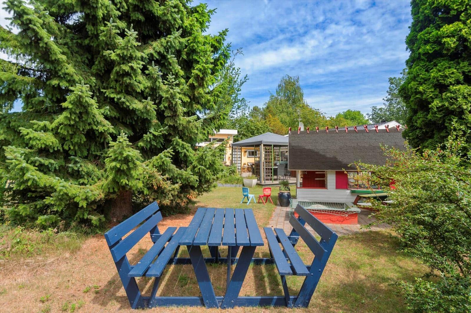Blauer Holztisch mit Bänken im Garten. Hintergrund: Haus mit Spielplatz und Bäumen.